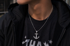 Person wearing a black jacket with a necklace featuring an anchor pendant.
