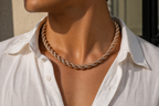 Person wearing a gold braided necklace with a white shirt.